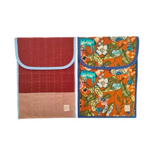 Puede incluir: Dos fundas de tela. Una es acolchada en burdeos y beige con un ribete azul claro. La otra tiene un estampado floral con ciervos turquesa sobre un fondo naranja, también con un ribete azul claro. Ambas tienen cierre de solapa.