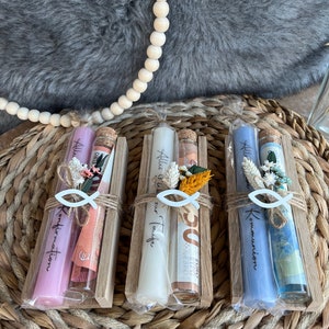 May include: Three gift sets in wooden holders, each containing a candle, a small glass bottle, and decorative elements. The candles are in shades of pink, white, and blue. The bottles have cork stoppers and are tied with twine.