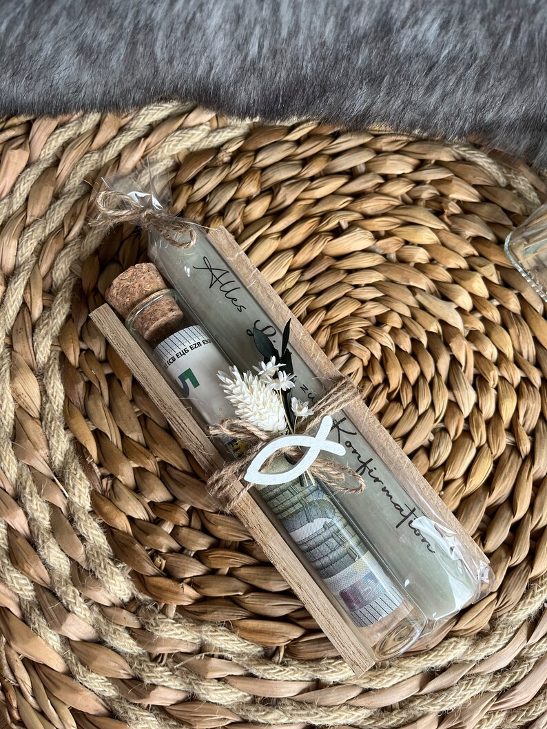 May include: A gift set in a wooden frame, featuring a glass tube with rolled-up currency, a small corked bottle, and a candle with text. The set is decorated with a white fish symbol and dried flowers, all tied with twine.