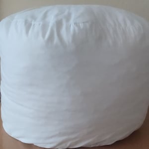 Puede incluir: Un puf redondo blanco con una funda de tela lisa.