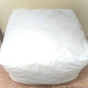 Puede incluir: Un puff blanco con una funda de tela lisa.