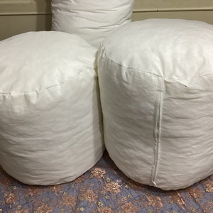 May include: Three white round poufs or ottomans made of fabric. The poufs are sitting on a patterned surface.
