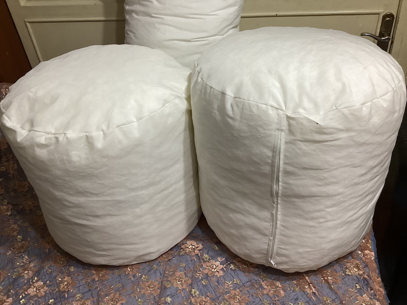 May include: Three white round poufs or ottomans made of fabric. The poufs are sitting on a patterned surface.