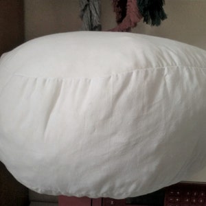 May include: A white round cushion with a gathered seam around the edge.