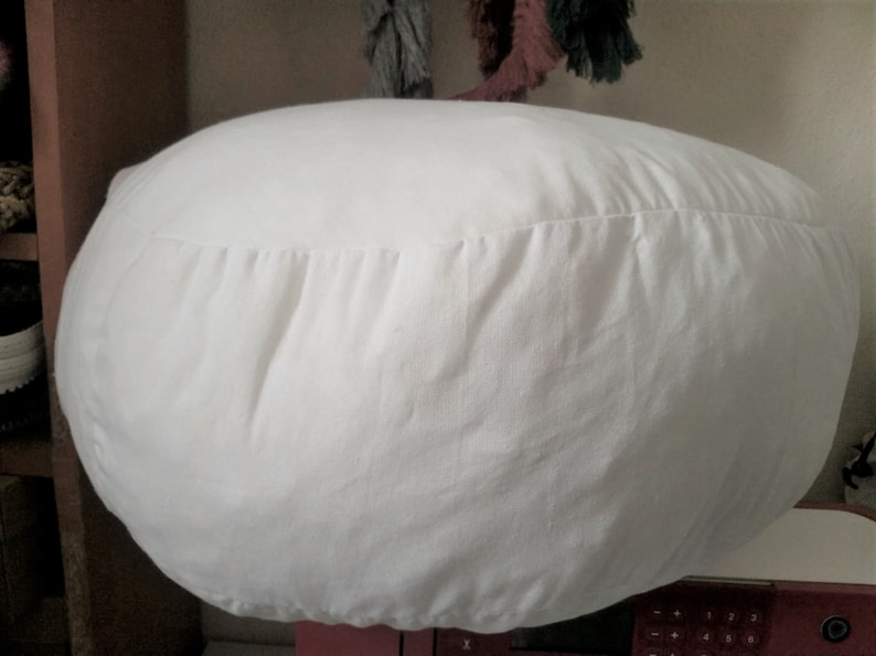 May include: A white round cushion with a gathered seam around the edge.