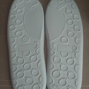 May include: A pair of white slipper soles with a textured pattern of small circles and a larger circle in the center. The soles are made of a soft, flexible material.