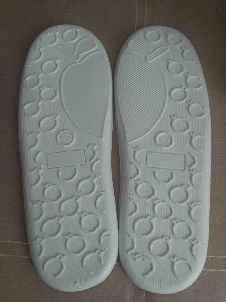 May include: A pair of white slipper soles with a textured pattern of small circles and a larger circle in the center. The soles are made of a soft, flexible material.