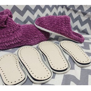 Puede incluir: Cuatro pares de suelas de zapatillas blancas y negras con una superficie texturizada. Tambi&eacute;n se muestran dos zapatillas de felpa morada.