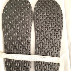 Könnte beinhalten: Ein Paar schwarze Schuheinlagen mit einem strukturierten Muster. Die Einlagen werden mit einem Maßband gemessen und zeigen eine Länge von 28 cm.