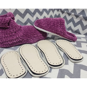 May include: Four pairs of purple fuzzy slippers with white soles. The slippers are on a gray and white chevron patterned fabric.