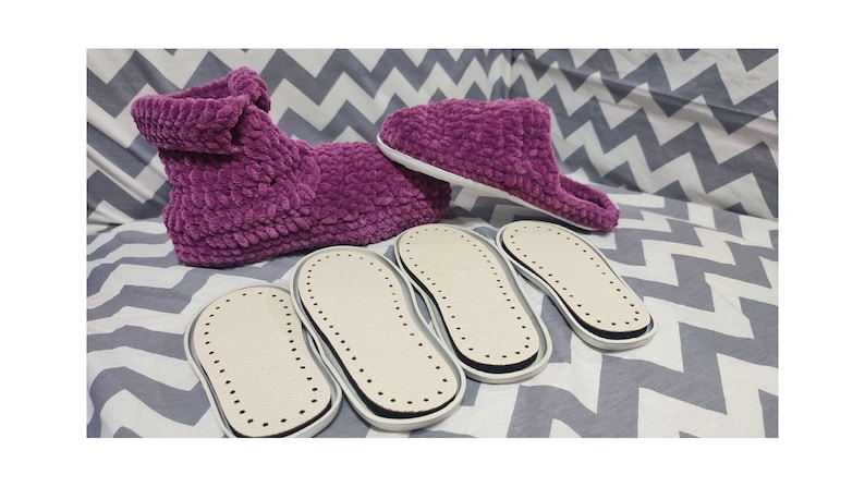 May include: Four pairs of purple fuzzy slippers with white soles. The slippers are on a gray and white chevron patterned fabric.