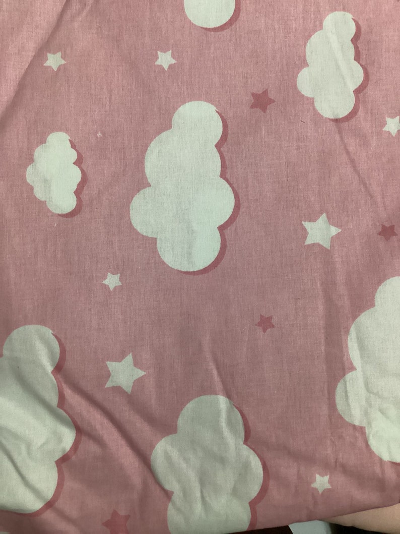 K&ouml;nnte beinhalten: Hellrosa Stoff mit einem sich wiederholenden Muster aus wei&szlig;en Wolken und Sternen. Die Wolken haben eine weiche, abgerundete Form, und die Sterne sind f&uuml;nfzackig. Der Stoff hat ein leicht strukturiertes Aussehen.