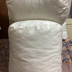 May include: Two white, round pillows stacked on top of each other. The pillows are made of a soft, white fabric and have a smooth, even texture.