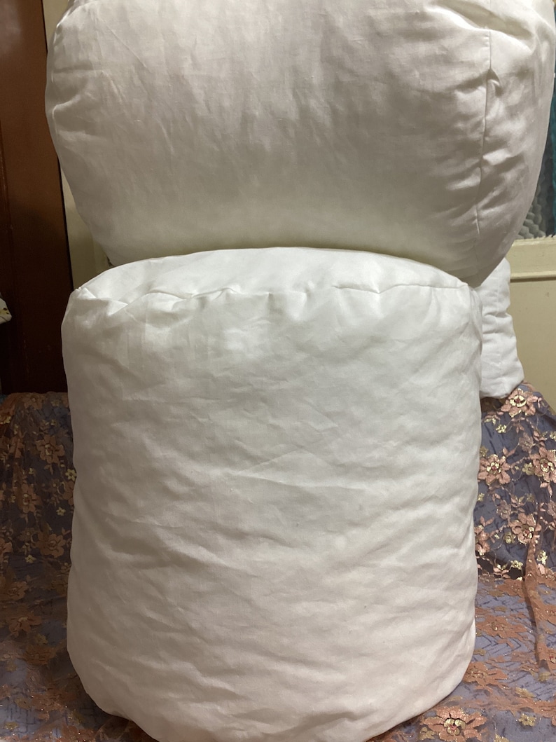 May include: Two white, round pillows stacked on top of each other. The pillows are made of a soft, white fabric and have a smooth, even texture.