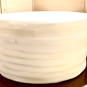 Puede incluir: Un maniquí de pastel redondo blanco con una superficie lisa ligeramente texturizada. El maniquí está hecho de poliestireno y tiene una parte superior ligeramente redondeada.