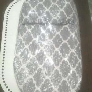 K&ouml;nnte beinhalten: Ein Babyprodukt mit grauem und wei&szlig;em Muster, verpackt in durchsichtiger Folie. Das Produkt hat eine abgerundete Form und ist auf einer wei&szlig;en, oval geformten Oberfl&auml;che mit einem gepunkteten Rand platziert. Das Muster ist ein sich wiederholendes geometrisches Design.