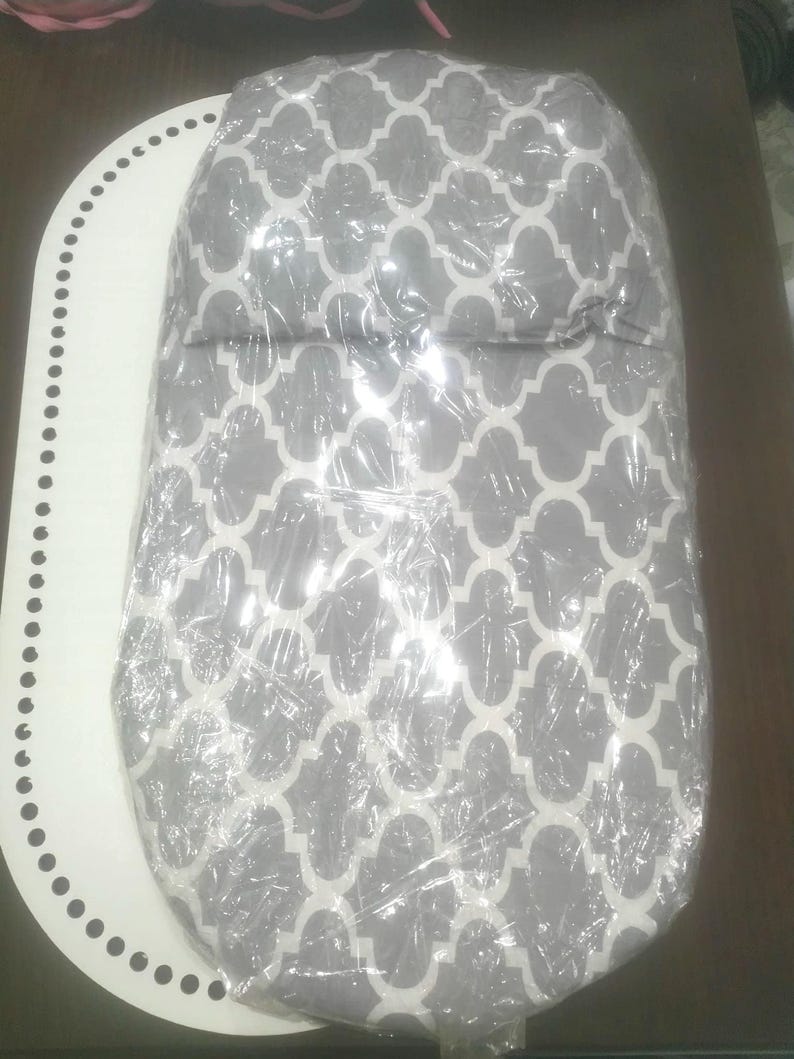 K&ouml;nnte beinhalten: Ein Babyprodukt mit grauem und wei&szlig;em Muster, verpackt in durchsichtiger Folie. Das Produkt hat eine abgerundete Form und ist auf einer wei&szlig;en, oval geformten Oberfl&auml;che mit einem gepunkteten Rand platziert. Das Muster ist ein sich wiederholendes geometrisches Design.