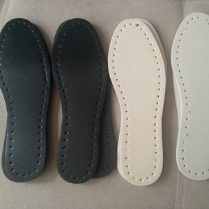 K&ouml;nnte beinhalten: Vier Ledereinlegesohlen in Schwarz und Off-White. Die Einlegesohlen sind oval geformt und haben eine Reihe kleiner L&ouml;cher am Umfang zum Ann&auml;hen. Zwei sind schwarz und zwei sind cremefarben.