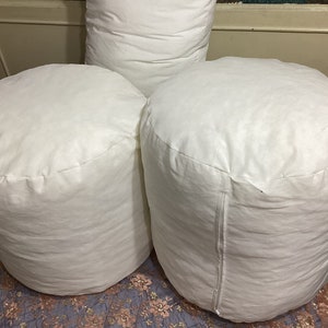 May include: Three white round poufs or ottomans made of fabric. The poufs are arranged in a triangular shape.