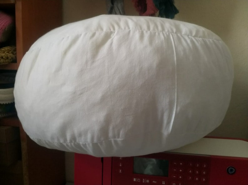 Puede incluir: Un coj&iacute;n grande, redondo y blanco con una costura en el centro. El coj&iacute;n est&aacute; encima de una m&aacute;quina de coser roja.