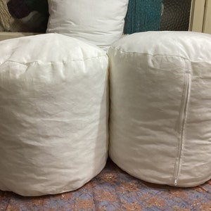 May include: Three white cylindrical pillows, two of which are lying on a patterned surface. The pillows are made of a soft, white fabric and have a smooth, rounded shape.