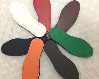 May include: A collection of colorful shoe insoles in various shades, including white, red, brown, green, navy, orange, and black. Each insole is oval-shaped with a series of small holes around the perimeter, suggesting they are designed for hand-stitching or crafting.