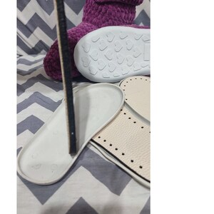 Puede incluir: Pantufla de color morado peluda con una suela blanca con un patr&oacute;n de corazones. La pantufla se muestra con dos suelas blancas con costuras negras.