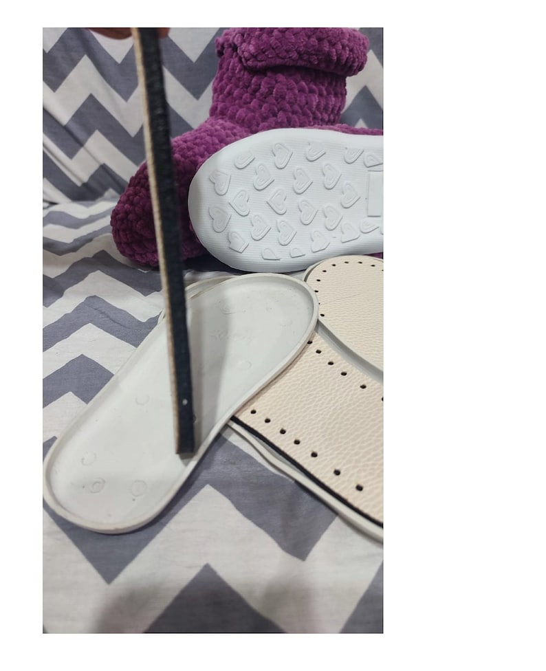 Puede incluir: Pantufla de color morado peluda con una suela blanca con un patr&oacute;n de corazones. La pantufla se muestra con dos suelas blancas con costuras negras.