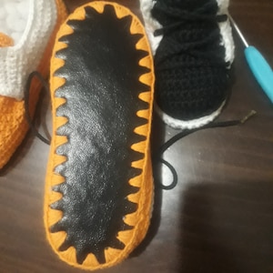 May include: Close-up of the bottom of a crocheted orange and white slipper with a black leather sole.