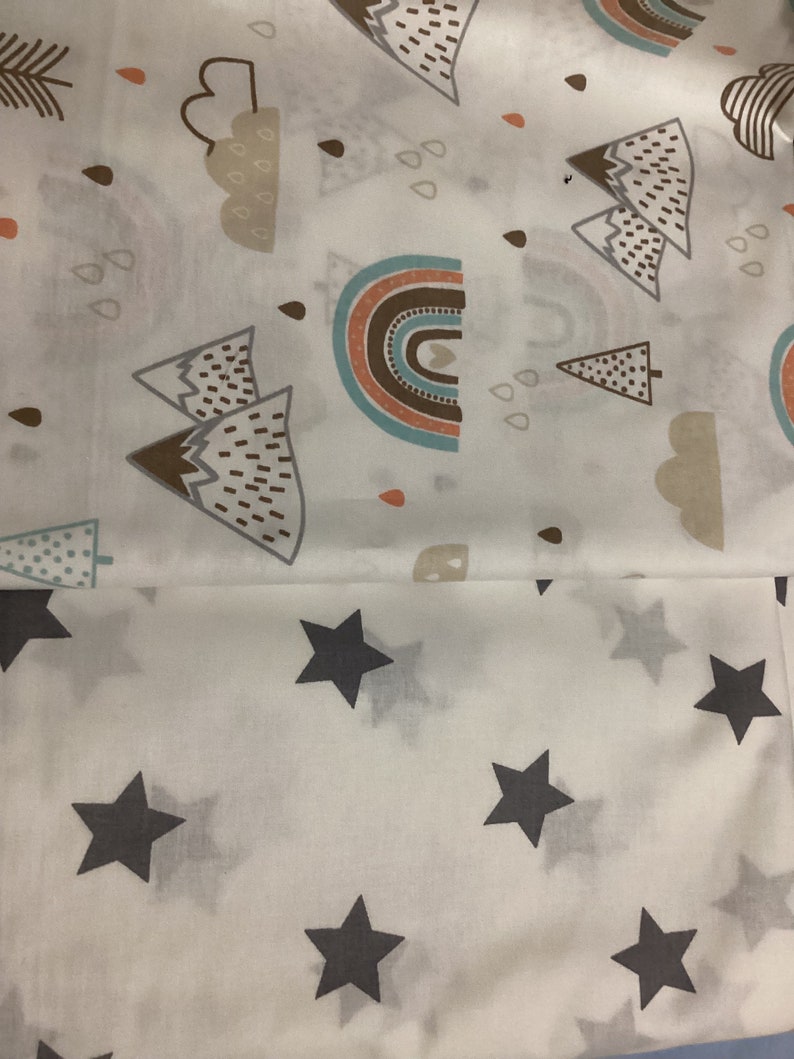 K&ouml;nnte beinhalten: Wei&szlig;er Stoff mit einem sich wiederholenden Muster aus grauen Sternen. Der obere Teil zeigt ein Design aus Regenbogen, Bergen, Wolken und Regentropfen in Braun-, T&uuml;rkis- und Oranget&ouml;nen. Geeignet f&uuml;r Babybettw&auml;sche oder Kinderzimmerdekoration.