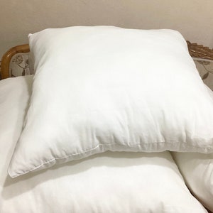 Peut inclure: Trois oreillers blancs empilés les uns sur les autres. Les oreillers sont faits d'un tissu blanc doux et ont une texture lisse et uniforme.