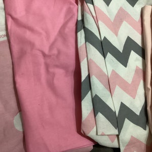 K&ouml;nnte beinhalten: Auswahl an gefalteten Stoffst&uuml;cken in Rosa-, Wei&szlig;- und Graut&ouml;nen. Ein St&uuml;ck hat ein Zickzackmuster, ein anderes einen Stern- und Monddruck. Der Text "100% COTTON" ist auf einem der Stoffe zu sehen.