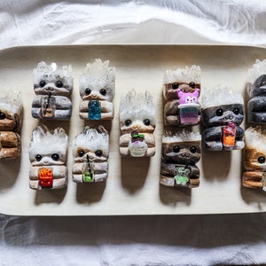 Könnte beinhalten: Eine Sammlung von 12 kleinen, mit Kristallen besetzten Figuren, die jeweils ein anderes Getränk halten. Die Figuren sind aus Harz gefertigt und haben verschiedene Farben und Designs.