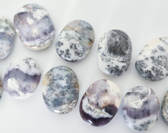 May include: A collection of eight smooth, oval-shaped, polished stones with a white, gray, and purple color pattern. The stones are arranged in a row on a white surface.