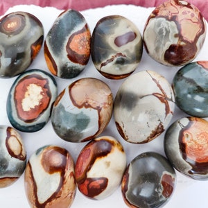 May include: A selection of polished stones in various colours and patterns. The stones are mostly oval, with shades of grey, brown, red, and cream. Some have circular or swirling patterns, while others feature more linear designs.