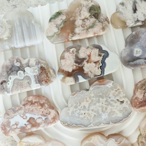 May include: A collection of agate cloud shaped stones in various shades of pink, white, and brown. The stones have a natural, organic look and are perfect for crystal healing or decoration.