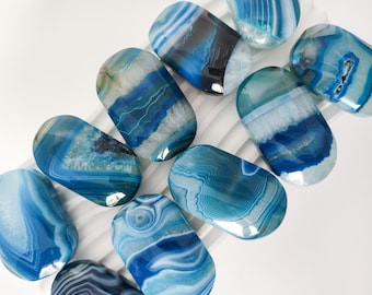 May include: A collection of ten oval-shaped blue agate stones with white and gray banding. The stones are smooth and polished.