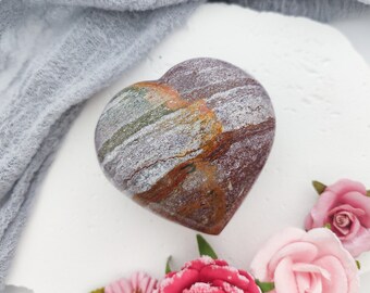 May include: A heart-shaped stone with a brown, white, and green marbled pattern. The stone is smooth and polished, and it has a natural, organic look.