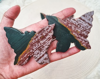 May include: Two green and brown butterfly-shaped polished stones with a white and gold marbled pattern.