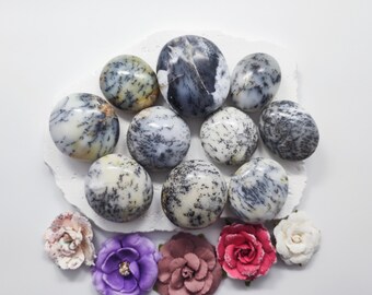 May include: A collection of ten smooth, round, polished stones with a white, gray, and black dendritic agate pattern. The stones are arranged in a circle on a white surface with small, colorful flowers around the edges.