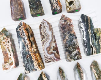 May include: A collection of 14 polished agate crystal points in various shades of brown, green, and white. The points are arranged in a random pattern on a white surface.