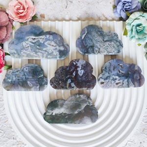 May include: Six agate cloud-shaped stones in shades of blue, green, and purple, arranged on a white circular platform with concentric rings.