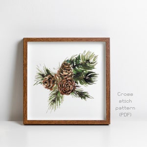 May include: A framed watercolour painting of pine cones and evergreen branches. The artwork features brown pine cones and green needles against a white background. The frame is made of wood. Text on the right side reads "Cross stitch pattern (PDF)".