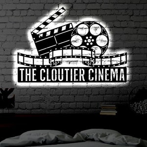 May include: A black and white illustration of a film reel and clapperboard with the text "The Cloutier Cinema" on a brick wall background.