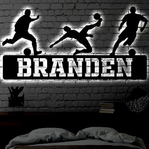 May include: Black and white silhouette of three football players with a nameplate that reads "BRANDEN" on a brick wall background.