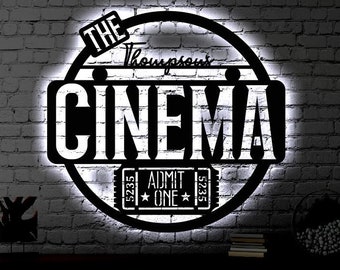 May include: A black and white metal sign with the text "The Thompson Cinema" and "Admit One" in a circle. The sign is illuminated with white light and is mounted on a brick wall.
