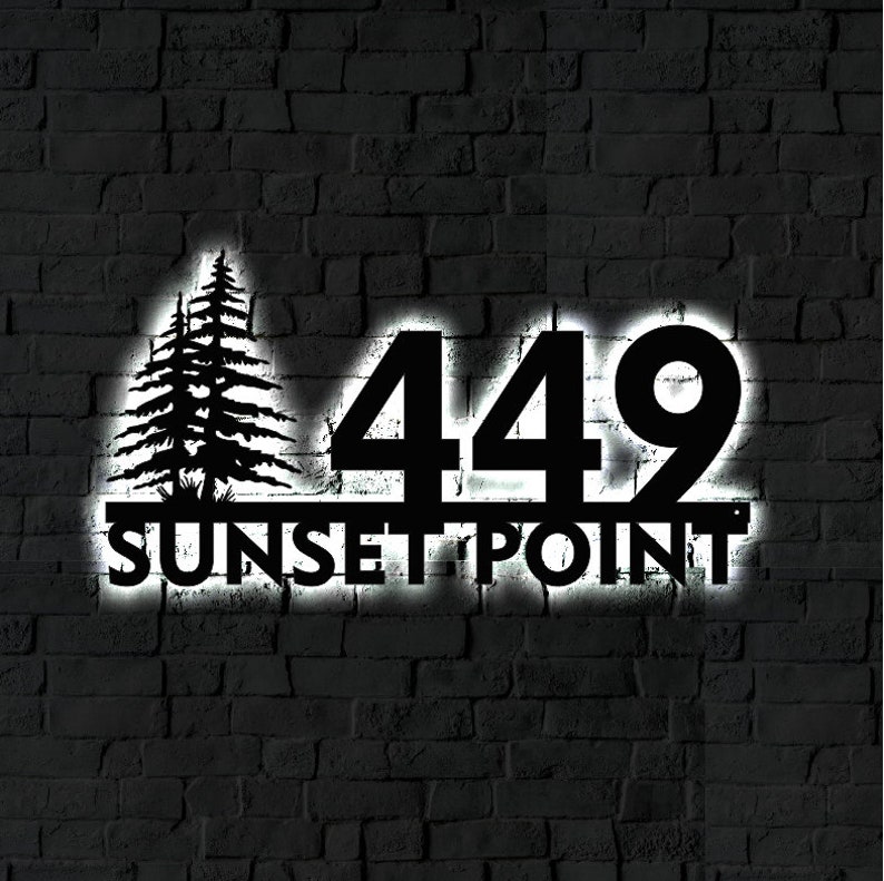 May include: Black metal house number sign with the number 449 and the words "SUNSET POINT" below. The sign is illuminated with white light and is mounted on a brick wall.