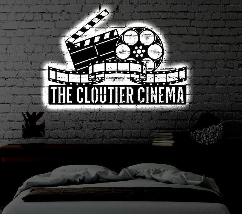 May include: A black and white illustration of a film reel and clapperboard with the text "The Cloutier Cinema" on a brick wall background.