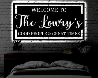 May include: A black and white sign with white text that reads "Welcome to The Lowry's Good People & Great Times". The sign is illuminated with white light and is hanging on a brick wall.