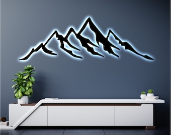 May include: Black metal mountain range wall decor with a white light behind it. The decor is mounted on a blue wall above a white entertainment center.